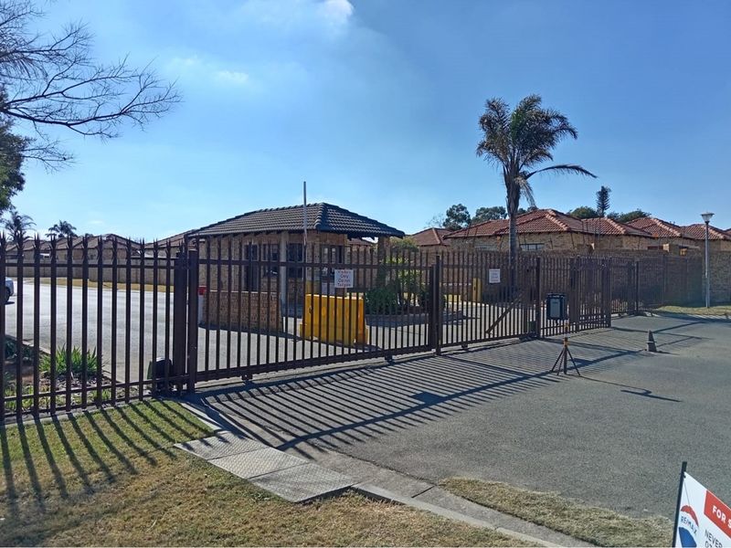 Secure gated entrance to the townhouse complex featuring a guard house, perimeter fencing, and paved access driveway.