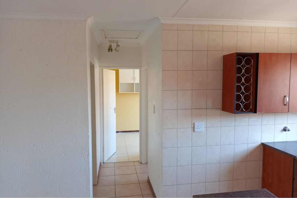 A view of a kitchen area featuring tiled splashbacks, built-in cabinetry with an integrated wine rack, and a connecting hallway leading to another room.