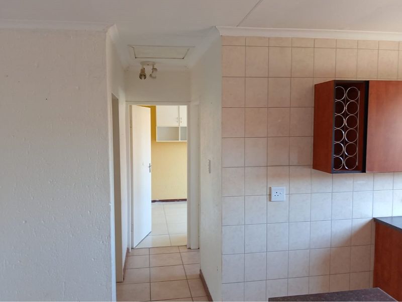 A view of a kitchen area featuring tiled splashbacks, built-in cabinetry with an integrated wine rack, and a connecting hallway leading to another room.