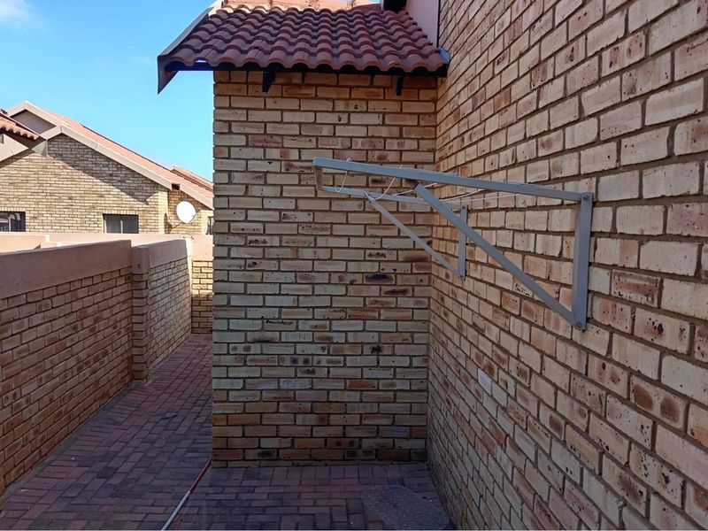 A side exterior view of the townhouse featuring face brick walls, a tiled roof section, and a paved walkway with a wall-mounted drying rack.