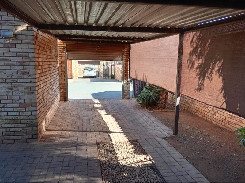 A covered carport area featuring brick walls, paved flooring, and metal roofing, providing secure off-street parking space.