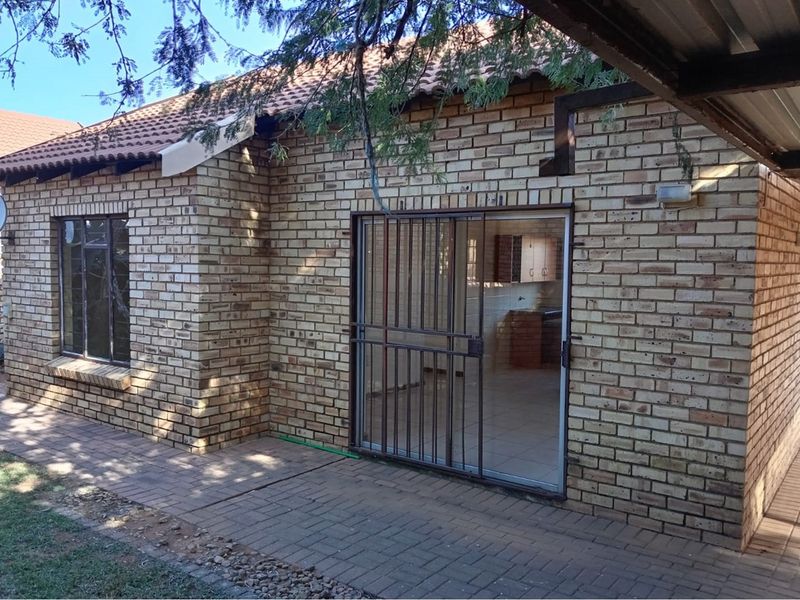Rear view of a face brick townhouse featuring a paved patio area, sliding glass door with security gate, and a tiled roof.
