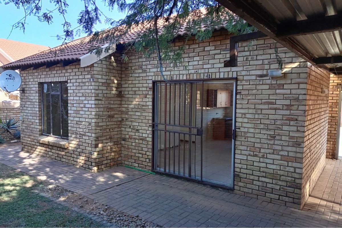 Rear view of a face brick townhouse featuring a paved patio area, sliding glass door with security gate, and a tiled roof.