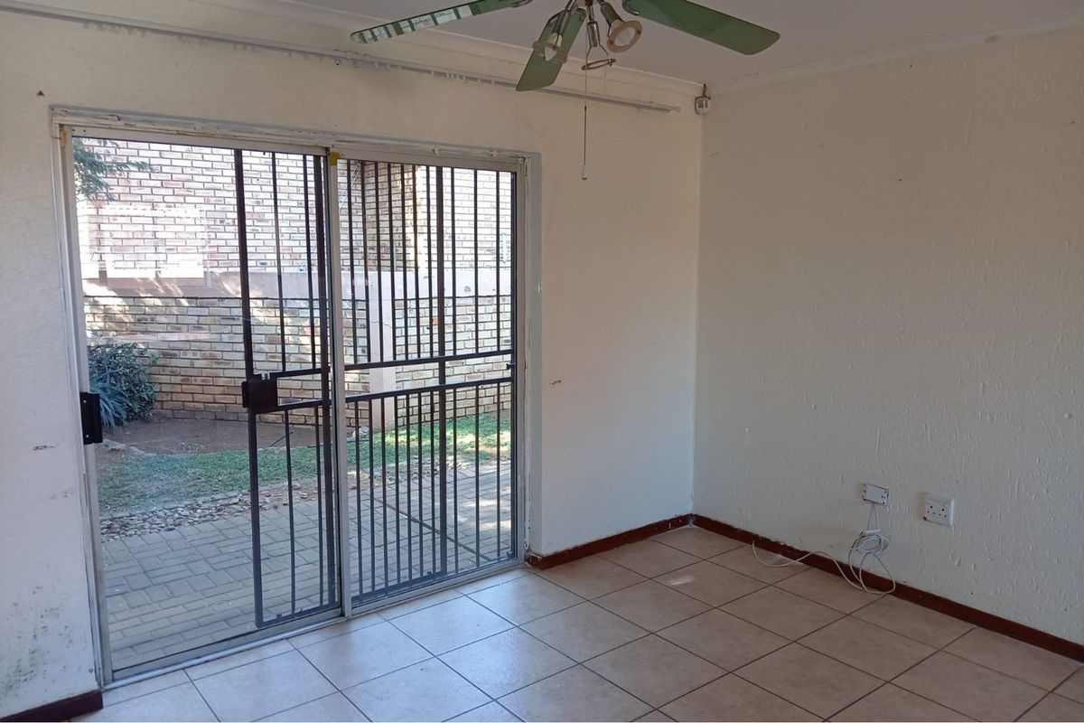 An empty living room featuring tiled flooring, a ceiling fan, and a sliding glass door with an integrated security gate leading to the exterior.