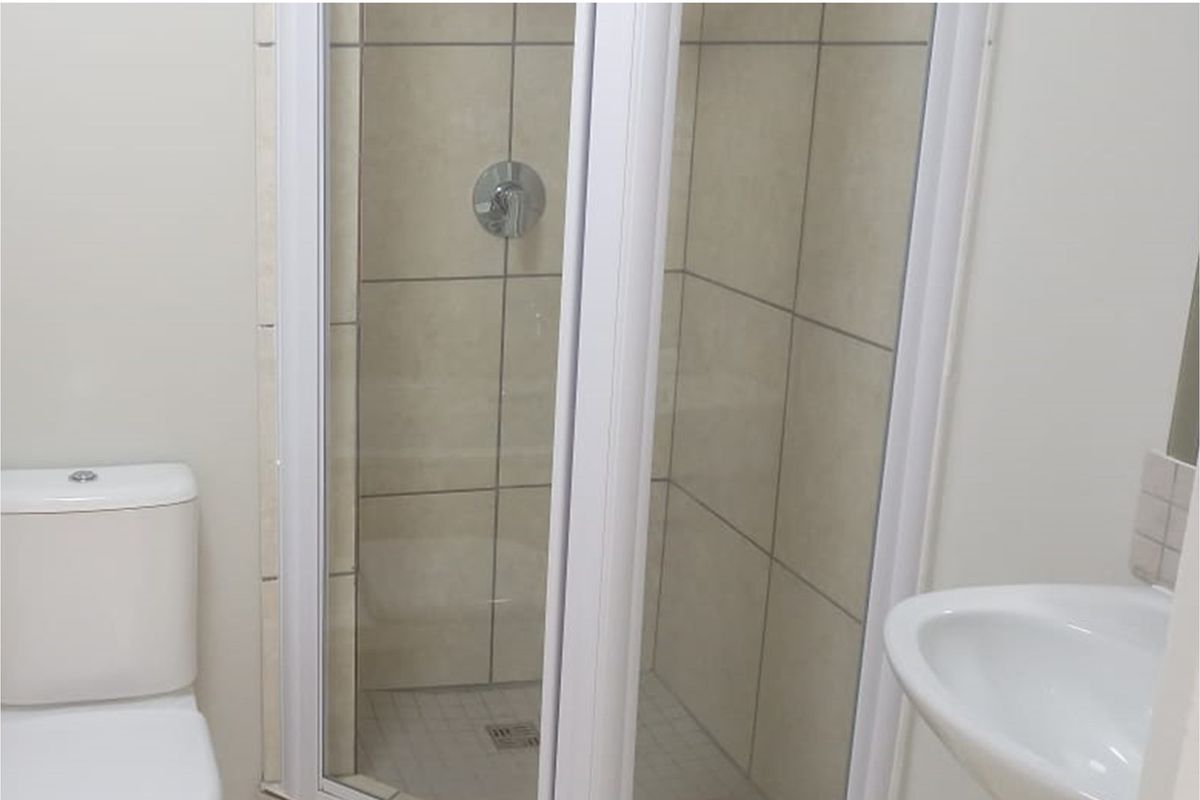 A functional bathroom featuring a shower enclosure, toilet, and washbasin with neutral wall tiling.