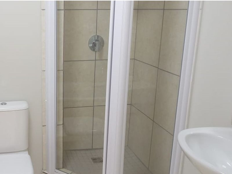A functional bathroom featuring a shower enclosure, toilet, and washbasin with neutral wall tiling.