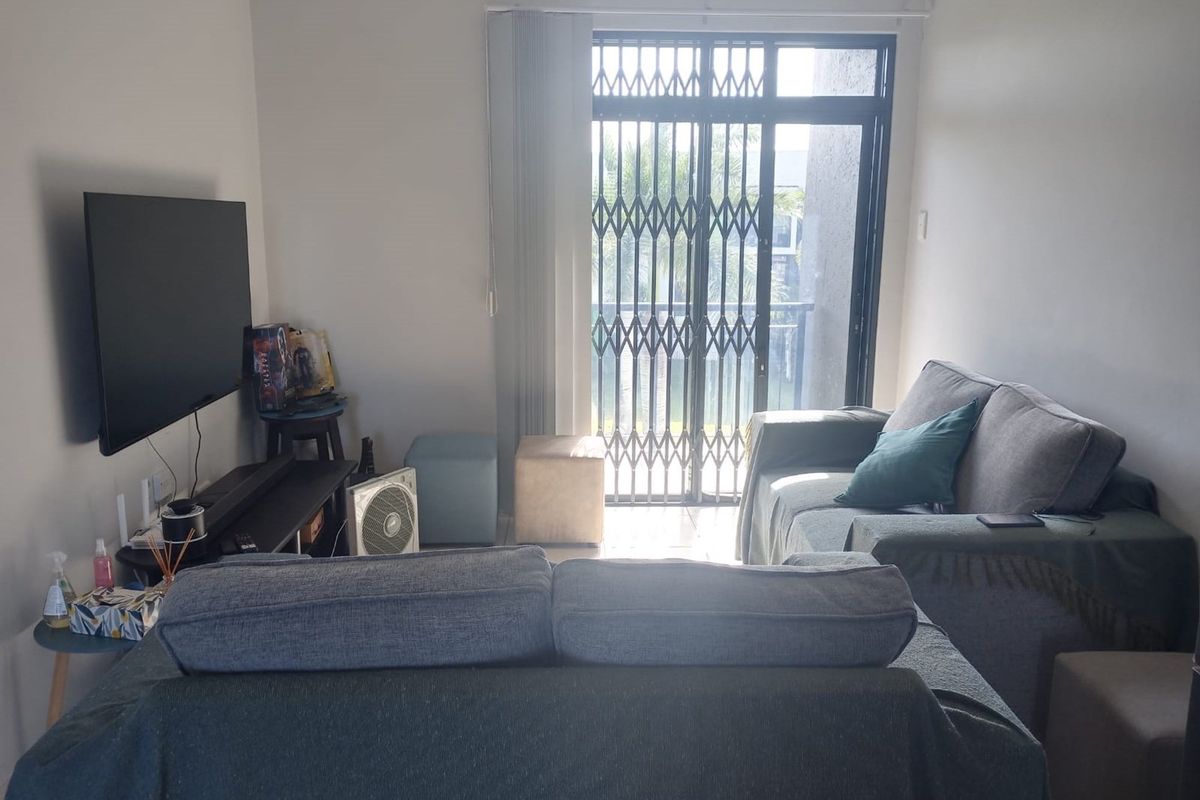 A living room featuring a sliding glass door with a security gate and vertical blinds, providing access to an outdoor area.