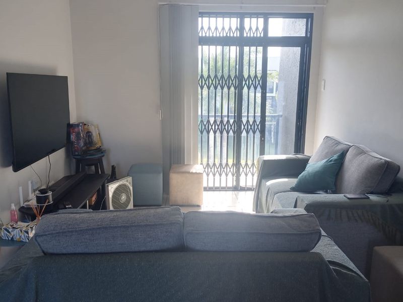 A living room featuring a sliding glass door with a security gate and vertical blinds, providing access to an outdoor area.