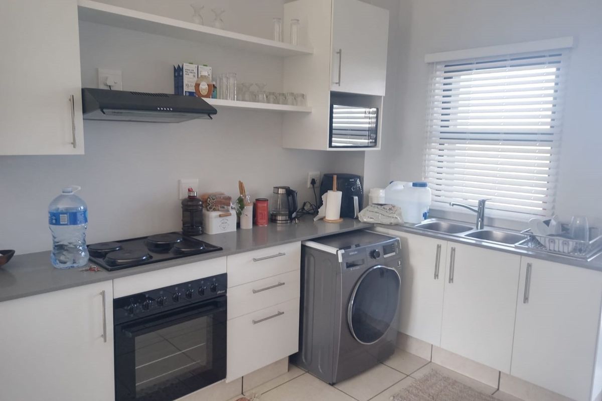 A functional kitchen featuring white cabinetry, grey countertops, an electric hob, built-in oven, extractor fan, and a double sink with venetian blinds.