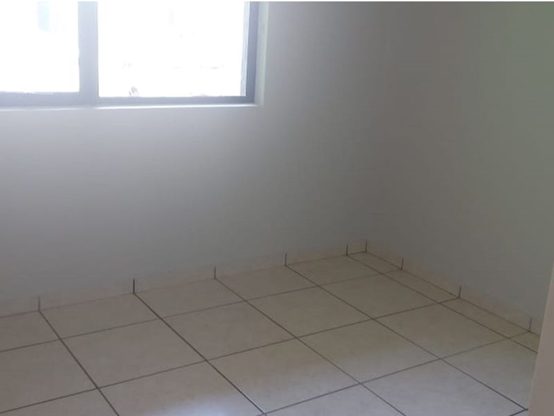 A simple, empty bedroom featuring neutral tiled flooring and a window, providing a blank canvas for personalization.