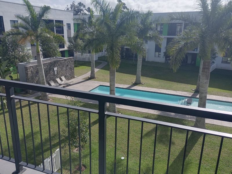 Elevated view of a communal apartment complex garden featuring a swimming pool, stone feature wall, and landscaped lawn area.