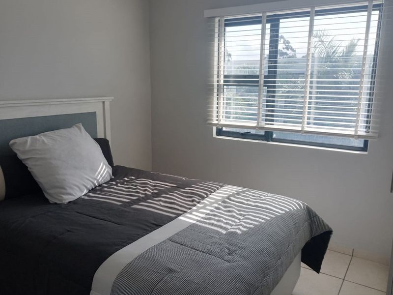 A well-lit bedroom featuring tiled flooring, a built-in wardrobe, and venetian blinds, offering a clean and functional living space.
