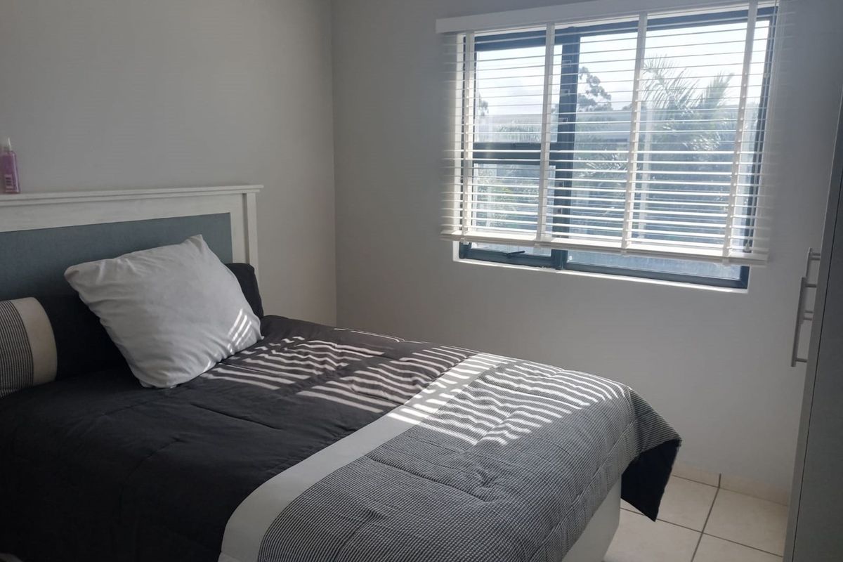 A well-lit bedroom featuring tiled flooring, a built-in wardrobe, and venetian blinds, offering a clean and functional living space.