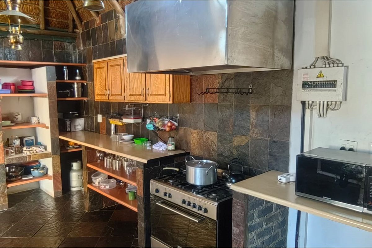 Rustic kitchen featuring stone-tiled walls, wooden cabinetry, a stainless steel extractor hood, and a gas stove with oven.