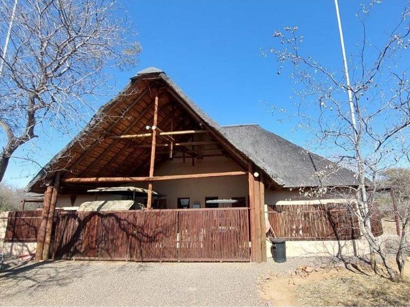 A rustic exterior view of a house featuring a traditional thatched roof, timber structural elements, and a wooden privacy fence.