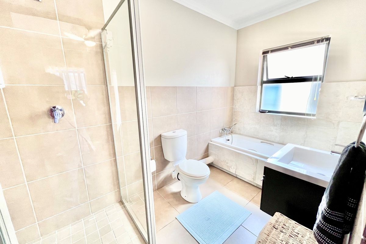 A well-maintained bathroom featuring a glass-enclosed shower, a built-in bathtub, a toilet, and a modern vanity unit with a basin.