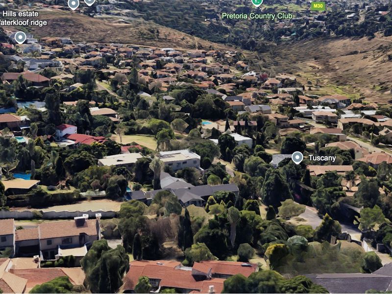 An aerial view of a residential neighborhood in Waterkloof Ridge, showing the surrounding landscape, mature trees, and established housing density.