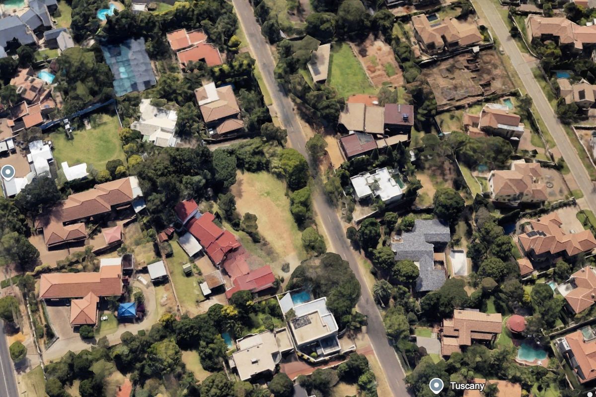 An aerial view of a residential neighborhood featuring established homes, mature trees, swimming pools, and paved street access.