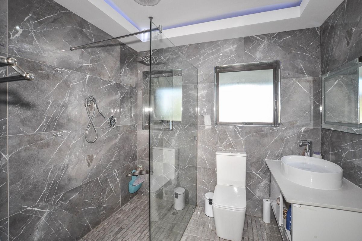 Modern bathroom featuring floor-to-ceiling grey marble-look tiling, a glass-enclosed walk-in shower with rainfall showerhead, and a contemporary vanity with vessel sink.