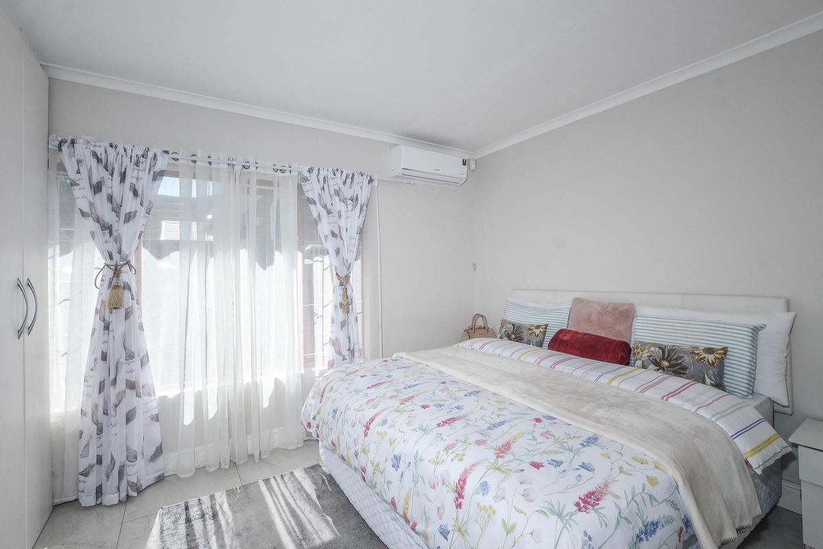 A bright and well-maintained bedroom featuring built-in cabinetry, tiled flooring, and a wall-mounted air conditioning unit.