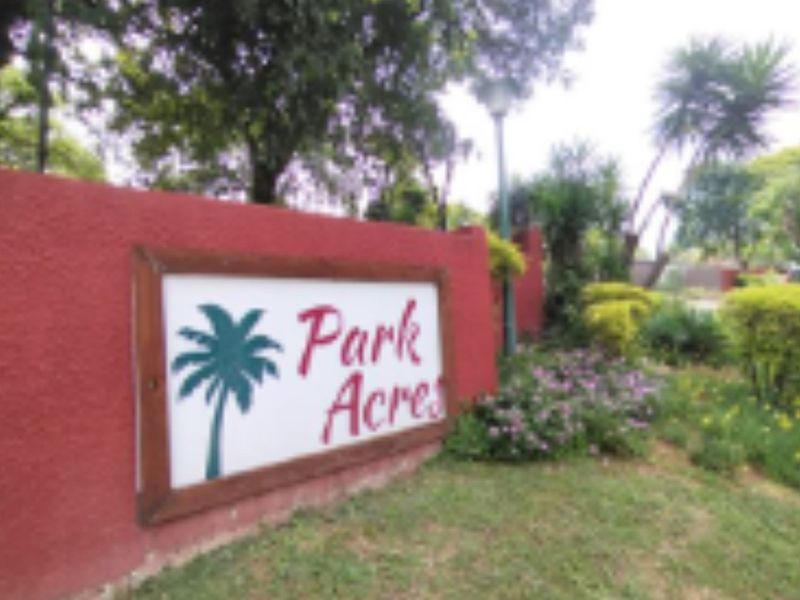 Entrance signage for Park Acres townhouse complex, featuring a red masonry boundary wall and established garden landscaping.