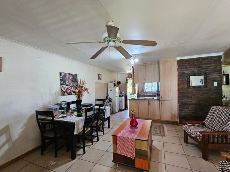 Open-plan living and dining area featuring tiled flooring, a ceiling fan, and a functional kitchen with built-in cabinetry and a brick feature wall.