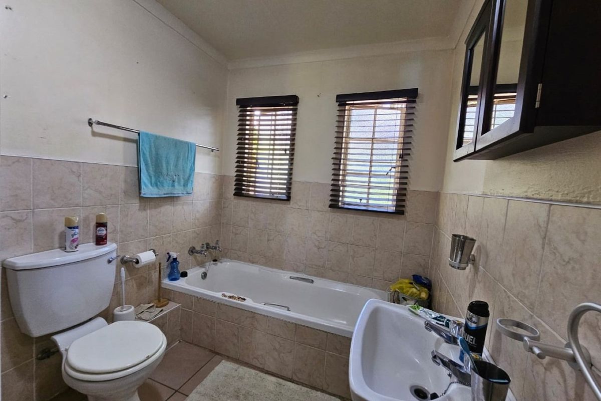 A functional bathroom featuring a built-in bathtub, pedestal sink, and toilet, finished with neutral wall tiles and fitted window blinds.