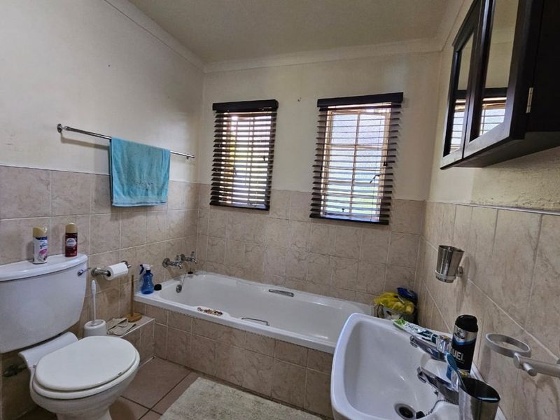 A functional bathroom featuring a built-in bathtub, pedestal sink, and toilet, finished with neutral wall tiles and fitted window blinds.