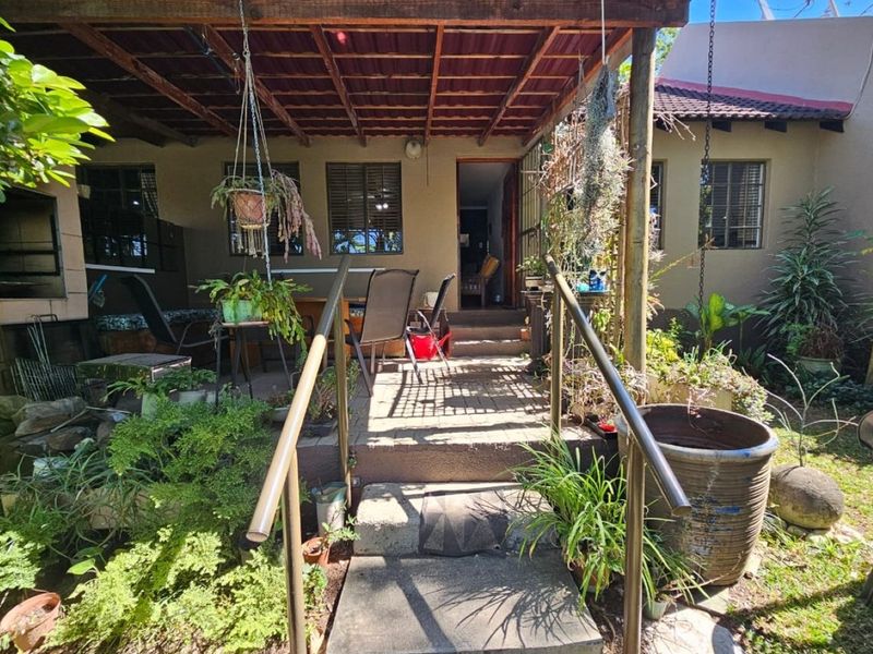 A covered patio area featuring a timber roof structure, concrete steps with metal handrails, and direct access into the main dwelling.