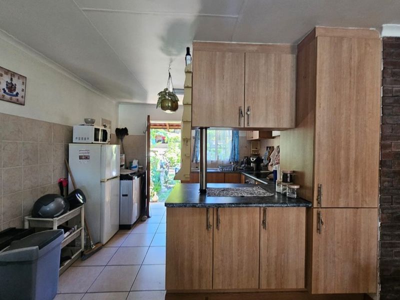 A functional kitchen featuring wood-look cabinetry, laminate countertops, and tiled flooring, with direct access to the rear garden area.