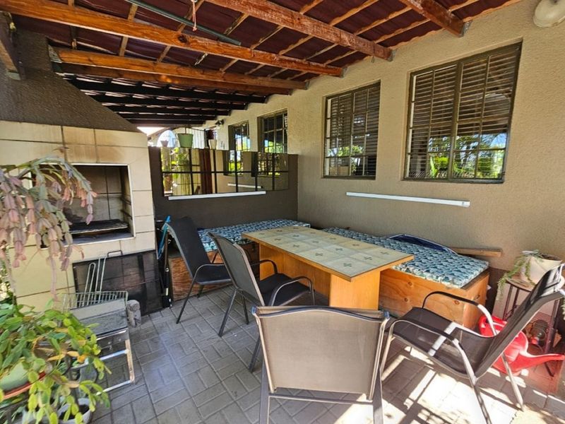 Covered patio area featuring a built-in brick braai, paved flooring, and timber roof structure, providing a functional outdoor entertainment space.