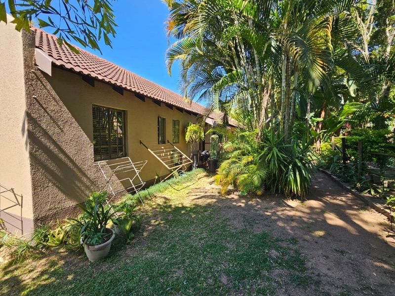 A view of the rear exterior of the townhouse, featuring a private garden area with mature palm trees and a tiled roof.