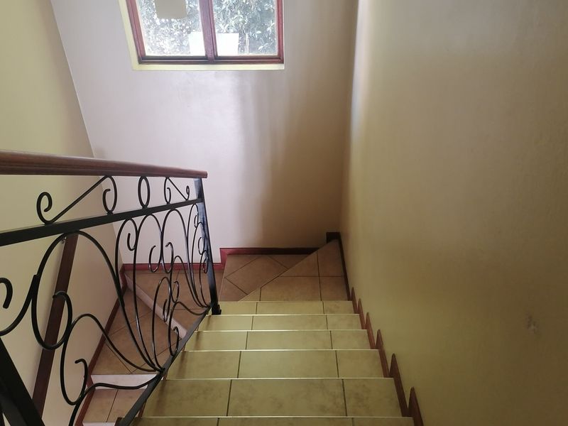 A staircase featuring tiled steps, a decorative wrought iron balustrade with a wooden handrail, and a window providing natural light.