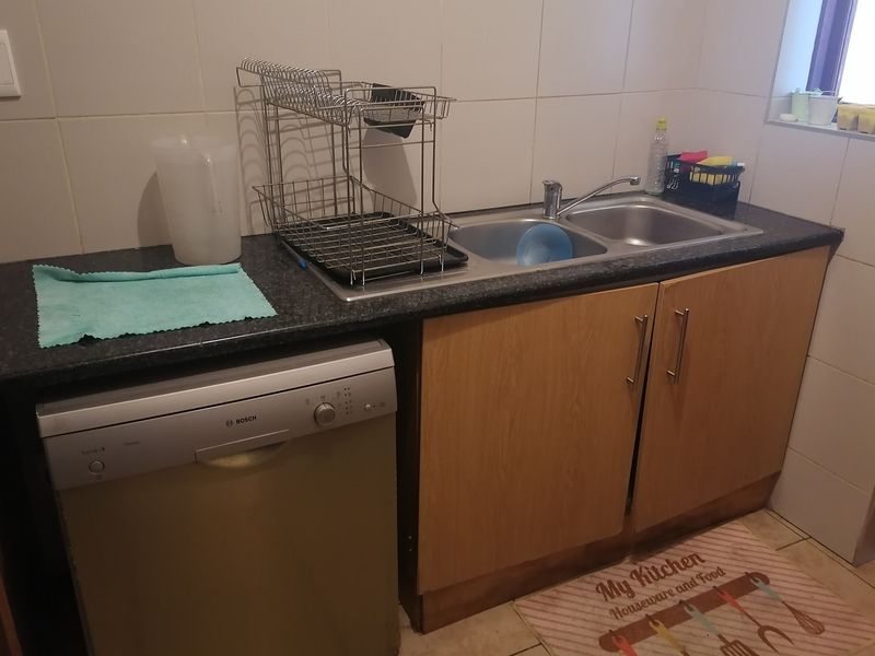 A functional scullery area featuring a double bowl stainless steel sink, laminate cabinetry, and space for a dishwasher with tiled splashback.