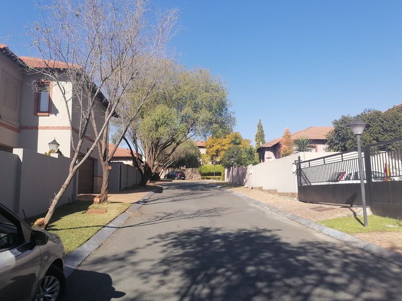 A view of the residential street showing the approach to the property with boundary walls, paved driveway, and metal security gate.