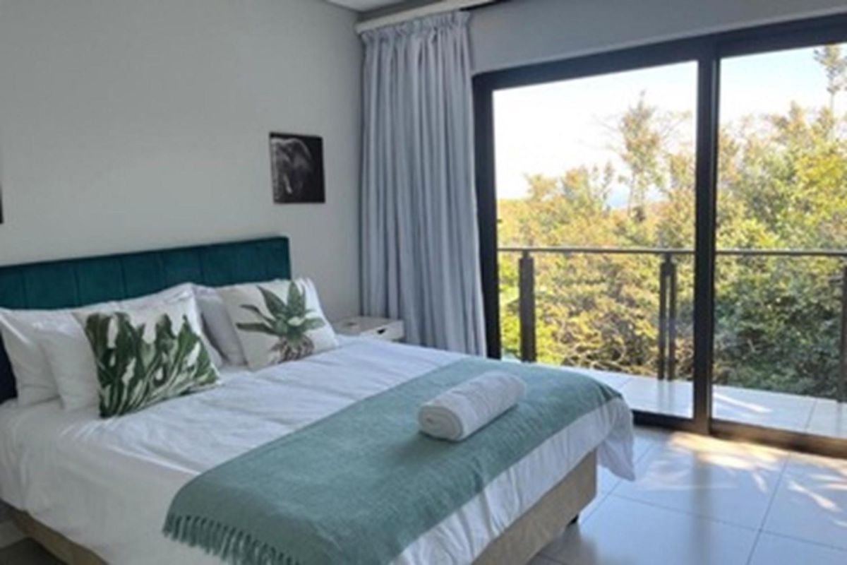 A bright bedroom featuring large sliding glass doors that open onto a private balcony with scenic treetop views.