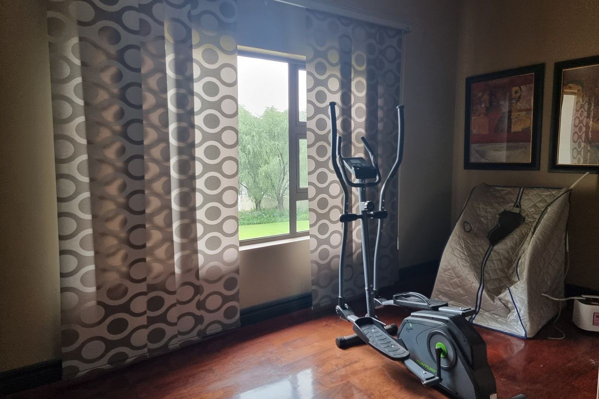 A bedroom featuring polished timber flooring and a large window with garden views, currently utilized as a home fitness space.