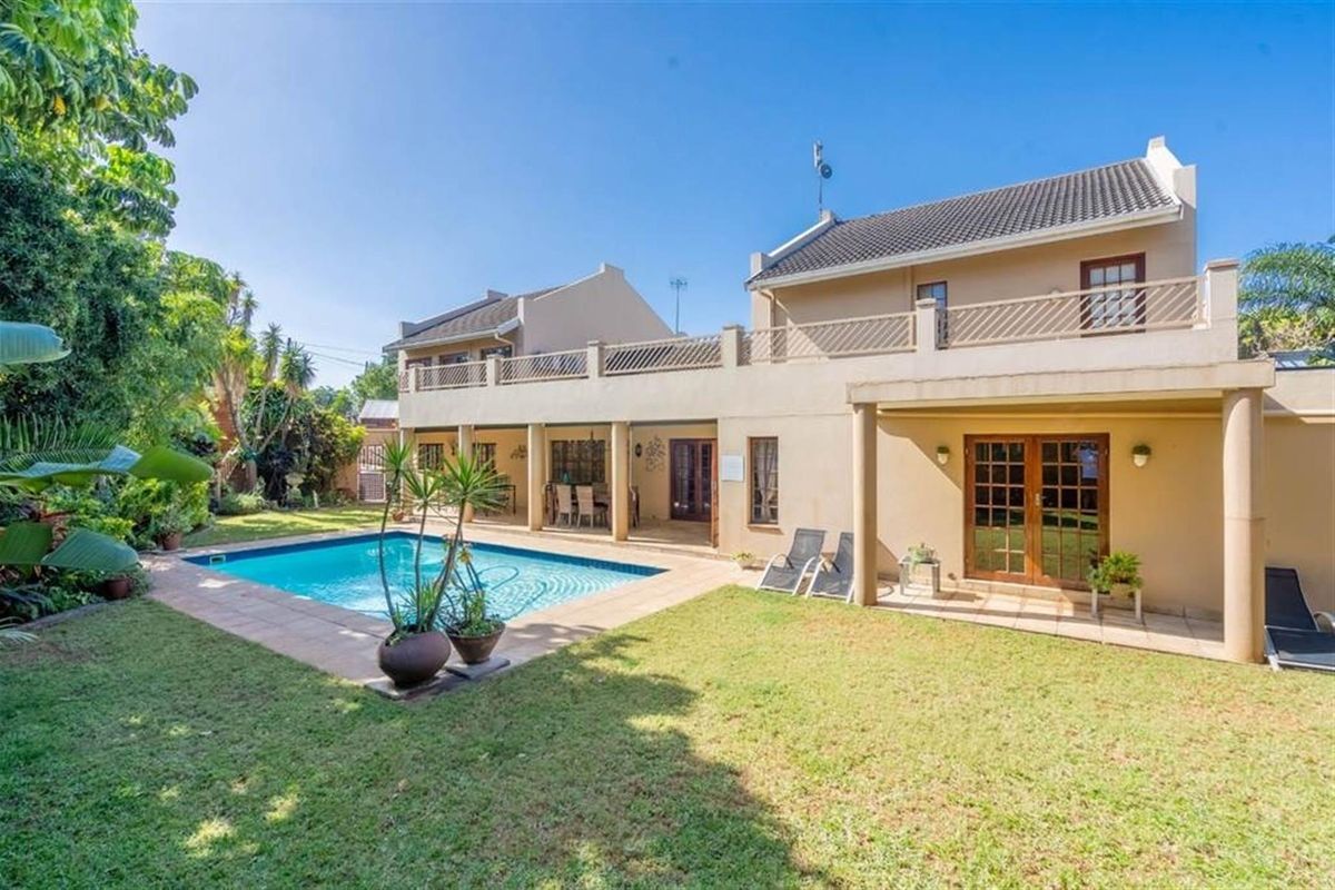 Rear view of the property featuring a swimming pool, a covered patio area, and a spacious garden with a balcony on the upper level.