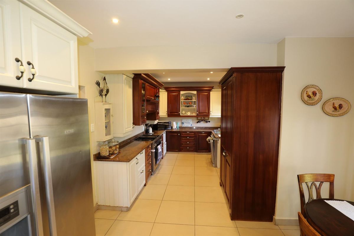A spacious kitchen featuring a mix of white and dark wood cabinetry, granite countertops, and tiled flooring with integrated appliance housing.