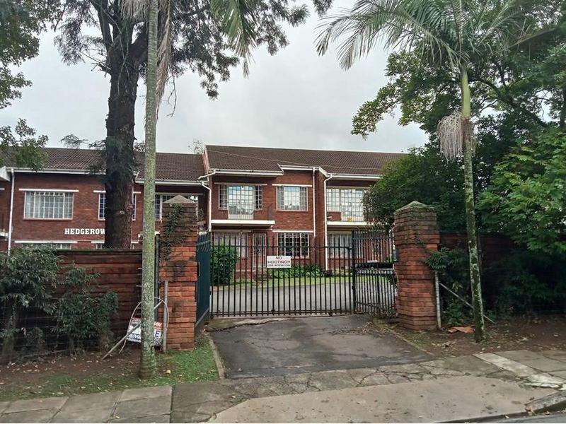 Front view of a brick apartment complex featuring a gated entrance, paved driveway, and established trees.
