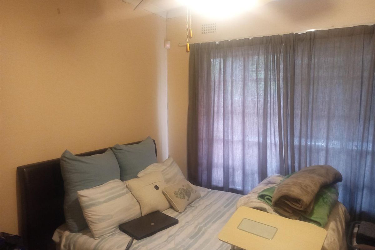 A bedroom featuring a ceiling fan and large window with curtain tracks, requiring cosmetic updates to the walls and ceiling finishes.