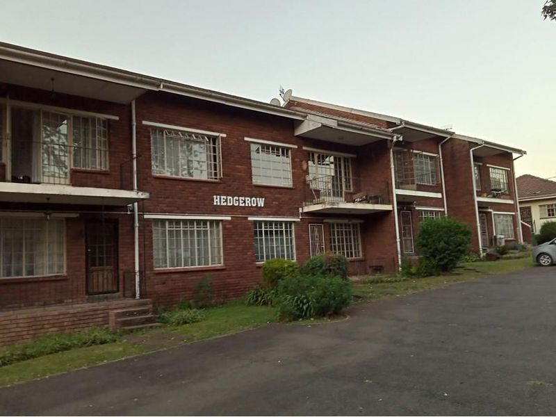 Exterior view of the Hedgerow apartment complex featuring a classic brick facade, security bars on windows, and private balconies.