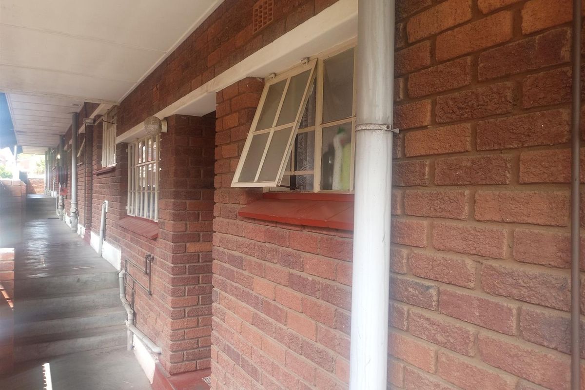 Exterior view of an apartment building walkway featuring exposed brick walls, metal window frames, and a concrete pathway.