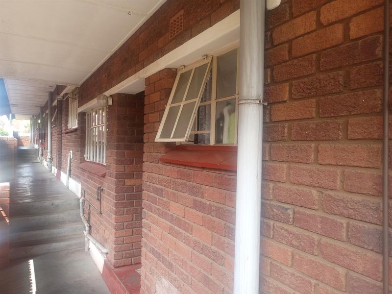 Exterior view of an apartment building walkway featuring exposed brick walls, metal window frames, and a concrete pathway.