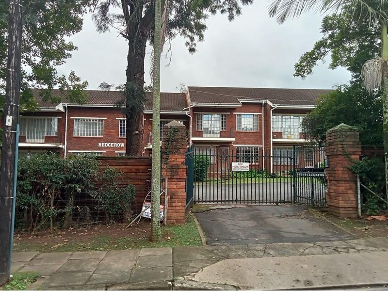 Front view of the Hedgerow apartment complex featuring a brick facade, tiled roof, and secure gated entrance with intercom access.