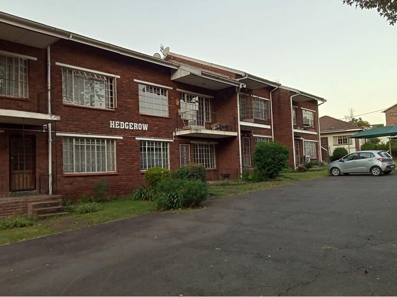 Exterior view of the Hedgerow apartment complex featuring a brick facade, security bars on windows, and an asphalt driveway.