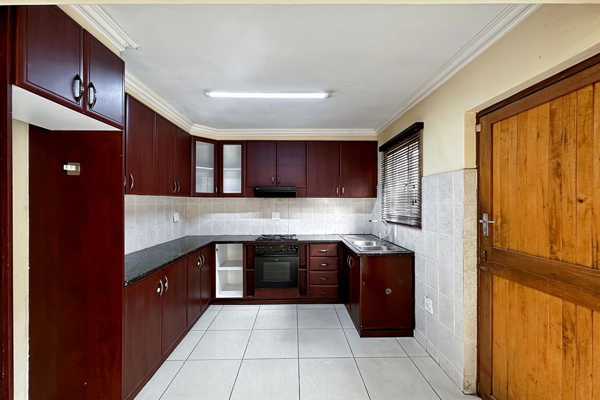 A functional kitchen featuring dark wood cabinetry, granite countertops, a built-in oven and hob, and tiled flooring.