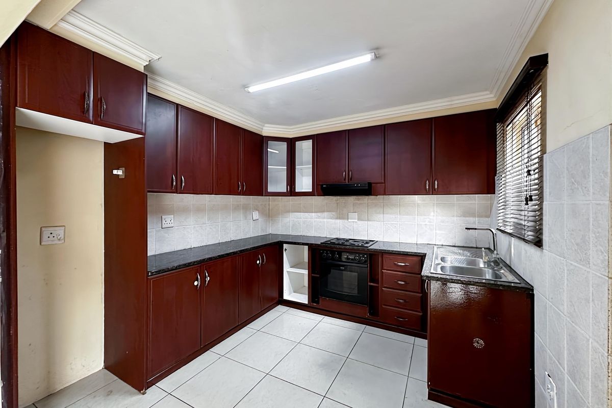 A functional kitchen featuring dark wood cabinetry, granite countertops, a built-in oven with hob, and tiled flooring.