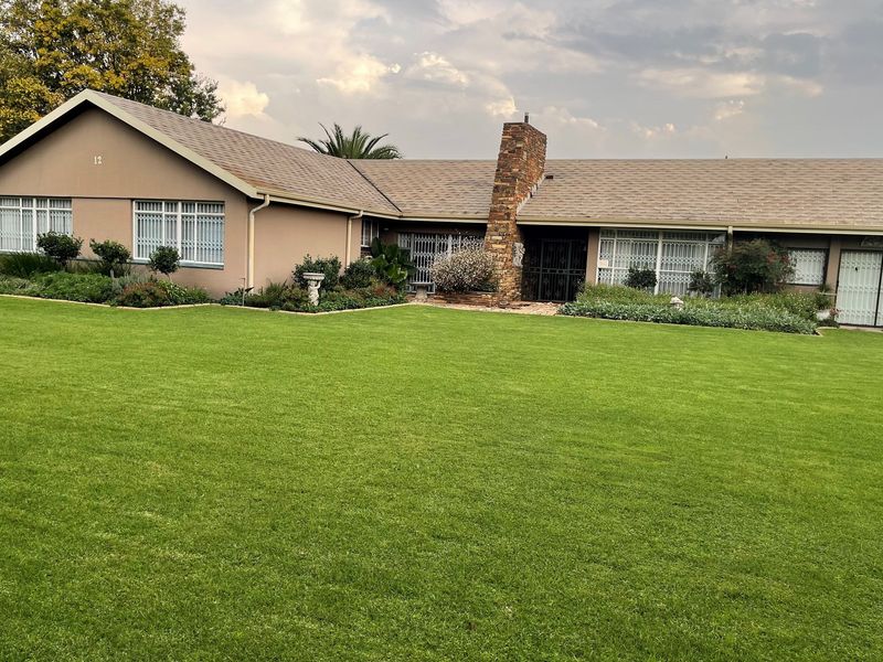 A well-maintained single-story residential property featuring a large manicured lawn, brick chimney, and secure window grilles.