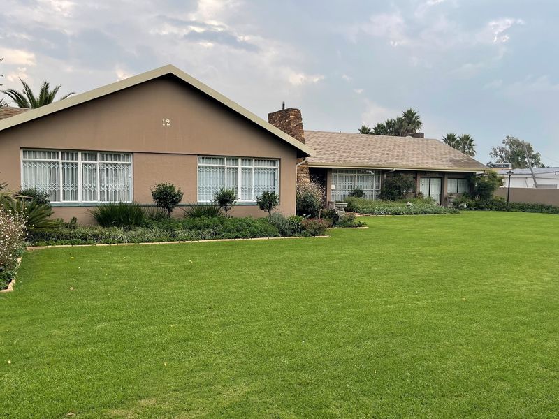 A well-maintained single-story residential property featuring a large manicured lawn, stone chimney, and classic architectural facade.